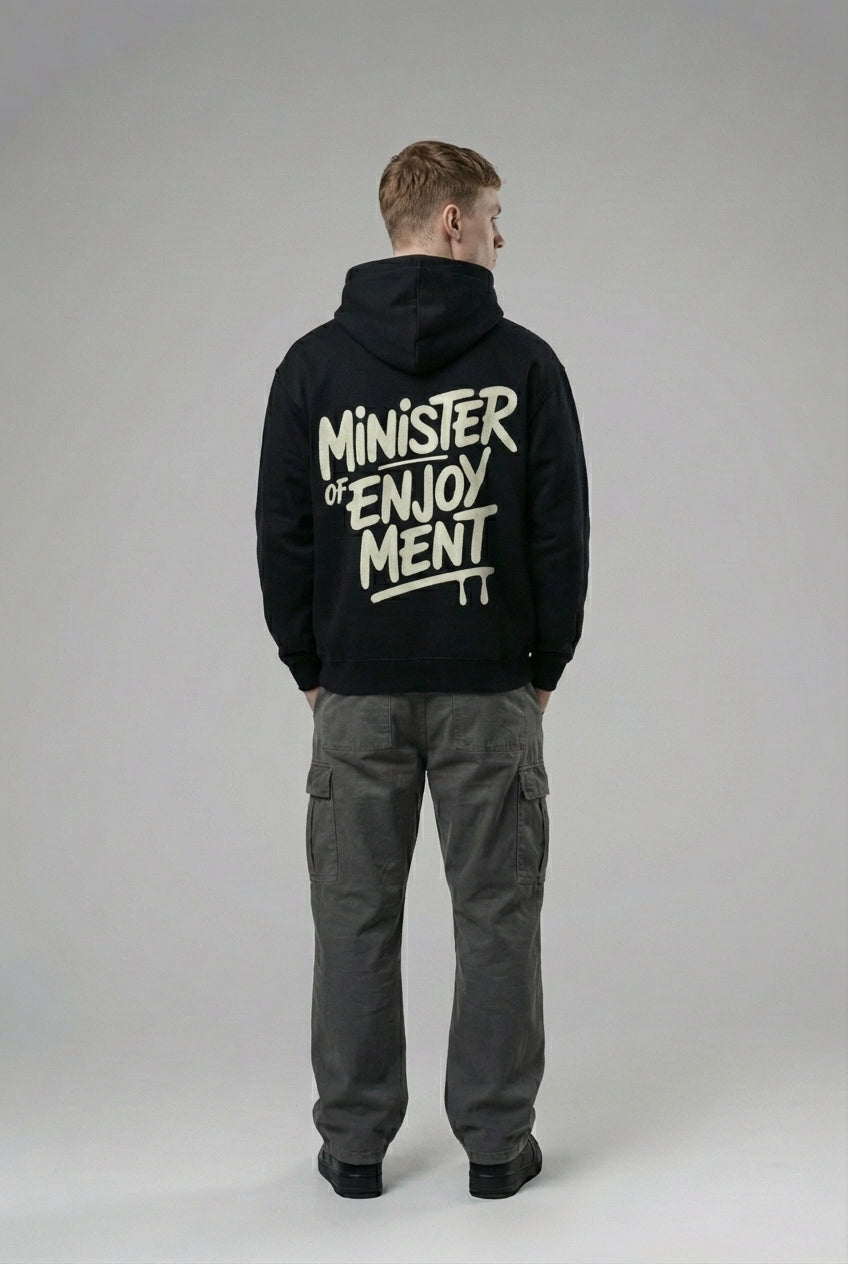 Back pose of the model wearing The Minister Of Enjoyment Oversized Hoodie- Black